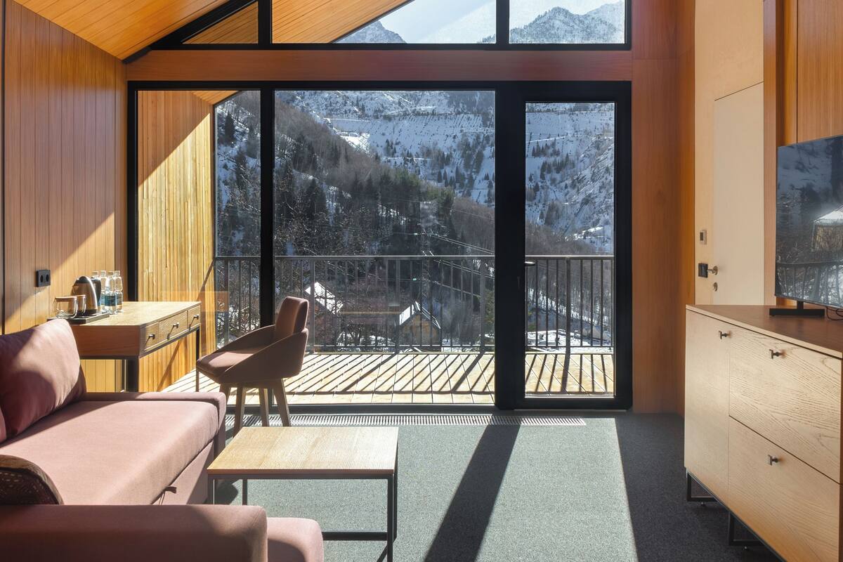 Un interior moderno con un balcón amplio, muebles de madera y vistas a montañas.