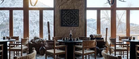 A cozy restaurant with wooden furniture and large windows offering a view of snow-covered mountains.