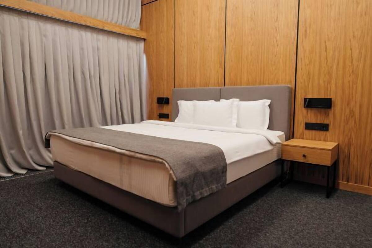 Habitación de hotel con cama, mesita de noche y panel de pared de madera.