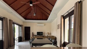 A spacious room with a high ceiling, a central island with seating, and large windows.