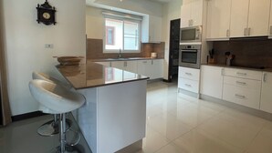 A modern kitchen with white cabinets, a central island with bar stools, a built-in oven, and a microwave.