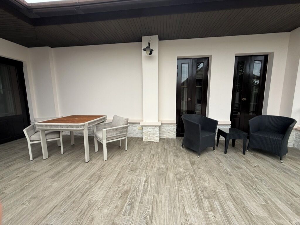 Un patio cubierto con una mesa y sillas de madera, una silla de mimbre oscuro y una pared de acento de piedra.