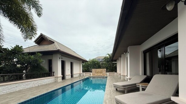A modern pool area with a rectangular pool, lounge chairs, and a stone-tiled deck.