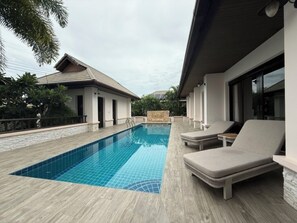 A modern pool area with a rectangular pool, lounge chairs, and a stone-tiled deck.