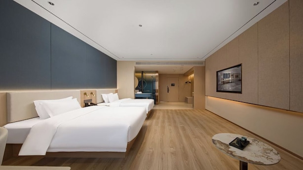 A modern hotel room with a large bed, bedside tables, a small round table, and a view of the city through the window. - Elong Anyue Hotel (Xi'an)