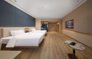 Una habitación de hotel moderna con una cama grande, mesitas de noche, una pequeña mesa redonda y vistas a la ciudad a través de la ventana.