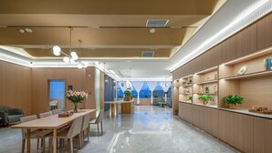 A modern hotel lobby with a long reception desk, a dining area with a wooden table and chairs, and a large window with a view of the city. - Elong Anyue Hotel (Xi'an)