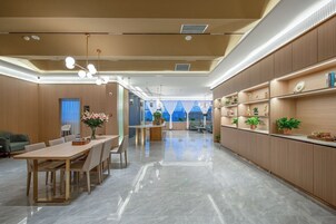 Un vestíbulo de hotel moderno con un largo mostrador de recepción, una zona de comedor con mesa y sillas de madera, y un gran ventanal con vistas a la ciudad.