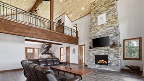 A spacious living area with a stone fireplace, leather seating, and a high ceiling with exposed beams.