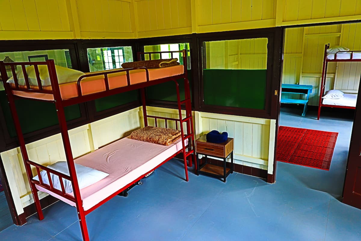 A bunk bed room with a wooden frame, a small wooden table, and a bench.