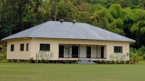 A single-story building with a flat roof, surrounded by lush greenery and a misty mountain backdrop. - Korovou Homestay Fiji (Naduri)