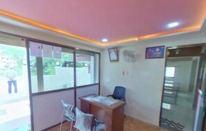 A reception area with a desk, chairs, a fan, and a glass door leading outside. - AkolaHostels (Akola)