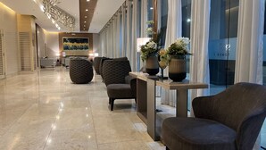 Eine moderne Lobby mit Marmorboden, einer Sitzecke mit gepolsterten Sesseln, einem Empfangsbereich und einem großen abstrakten Gemälde an der Wand.
