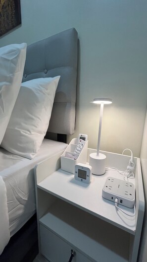 A neatly made bed with white bedding, a bedside table with a lamp, a power strip, and a digital clock. - Modern 1BRM apartment, Pool, Fast Wifi, Netflix, steps from MOA, Bars, Transport (Pasay)