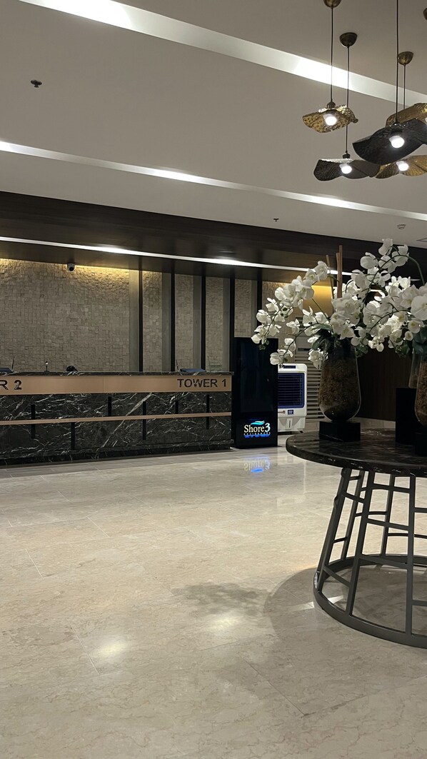 A hotel lobby with a reception desk labeled "TOWER 1" and "R2", a marble floor, and a large vase with white flowers. - Modern 1BRM apartment, Pool, Fast Wifi, Netflix, steps from MOA, Bars, Transport (Pasay)