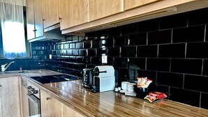 Une cuisine moderne avec des meubles en bois, un dosseret de carreaux noirs, une machine à café et un paquet d’en-cas posé sur le comptoir.