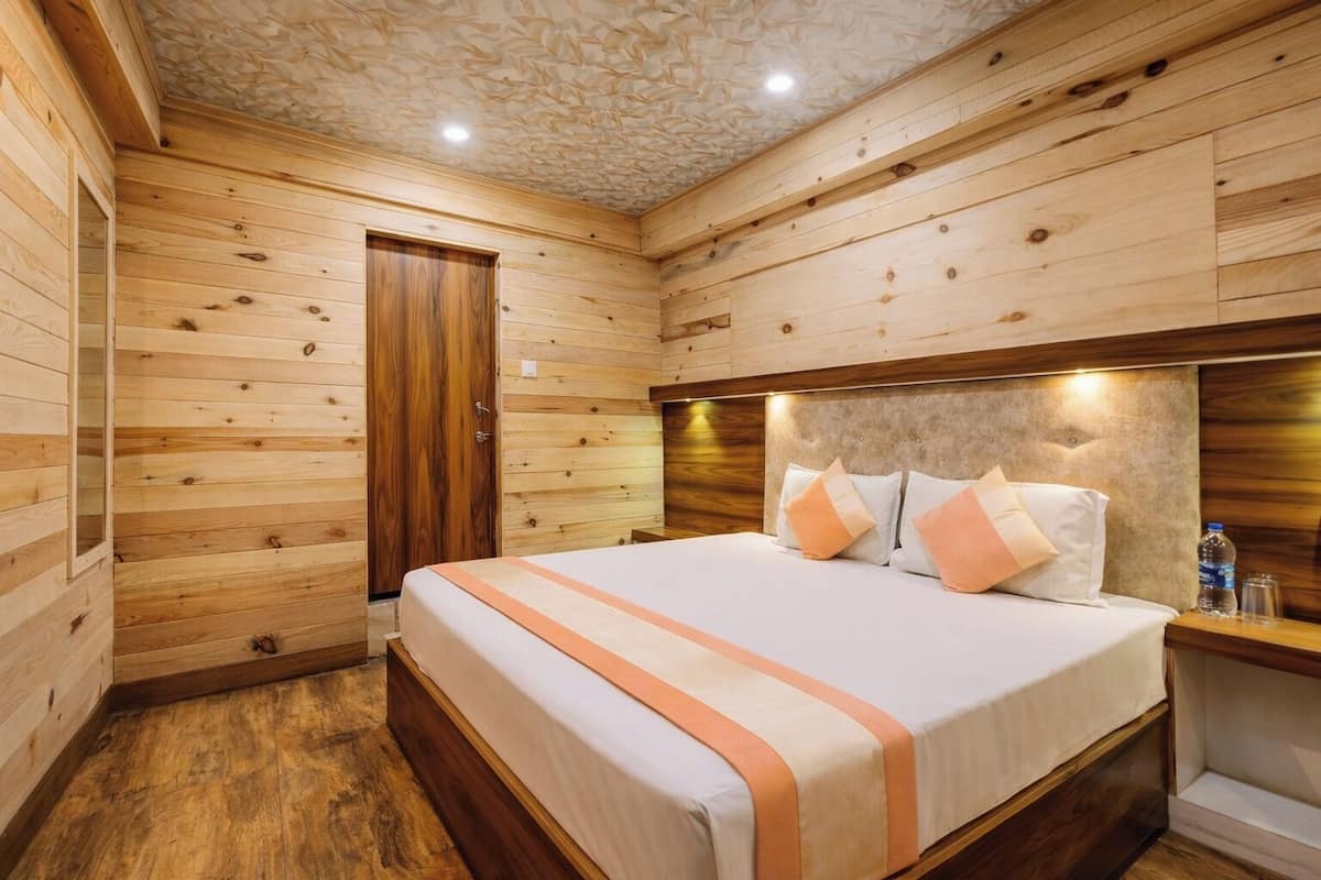 Una habitación con paneles de madera, una cama, una puerta de madera y una mesita de noche con una botella de agua.
