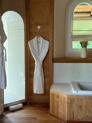 A bathroom with a wooden floor, a white bathtub, a wooden wall with a towel rack, and a window with a view of greenery. - Cozy Chalet w/Fireplace, Patio & Barbecue. Pet Friendly! (Gex)