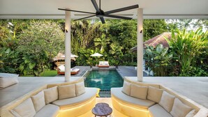 Ein moderner Außenlounge-Bereich mit Pool, umgeben von üppiger Vegetation und einem Deckenventilator.