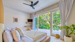 Een moderne slaapkamer met een groot bed, een plafondventilator, een televisie en uitzicht op weelderige begroeiing.
