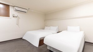 Ein Hotelzimmer mit zwei Betten, Holzboden, Wand-Klimaanlage und einem kleinen Nachttisch mit Lampe.