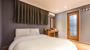 Ein ordentlich bezogenes Bett in einem Hotelzimmer mit einem Holztisch, einem Spiegel und einer Tür mit einer Milchglasplatte.