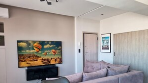 A modern living room with a large flat-screen TV, a grey sofa, and a dining table. - Athens Heart Acropolis Balcony (Athens)