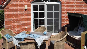 A brick house with a red-tiled roof, a large arched window, and a patio with wicker furniture and a table. - Vacation home Iljo in the fishing village of Greetsiel, Frisian coziness, 4 persons (Krummhörn)