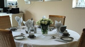 A dining table set with plates, cups, and a vase of flowers, surrounded by wicker chairs. - Vacation home Iljo in the fishing village of Greetsiel, Frisian coziness, 4 persons (Krummhörn)