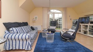 A living room with a striped sofa, a black leather chair, a blue rug, and a white cabinet with a TV. - Vacation home Iljo in the fishing village of Greetsiel, Frisian coziness, 4 persons (Krummhörn)