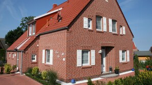 A red brick house with a sloped roof, white shutters, and a small garden with plants and a blue globe ornament. - Vacation home Iljo in the fishing village of Greetsiel, Frisian coziness, 4 persons (Krummhörn)