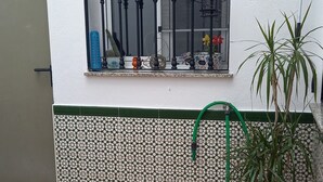 A potted plant next to a window with a metal grill, a tiled wall with a green border, and a tiled floor. - Andalusia Tourist Accommodation (Córdoba)