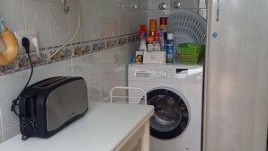 A compact kitchen with a microwave, a Bosch washing machine, a refrigerator, and a small table with a toaster. - Andalusia Tourist Accommodation (Córdoba)