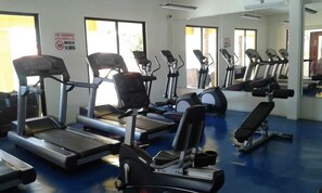 Une salle de sport équipée de tapis de course, de vélos elliptiques et d’un banc de musculation.