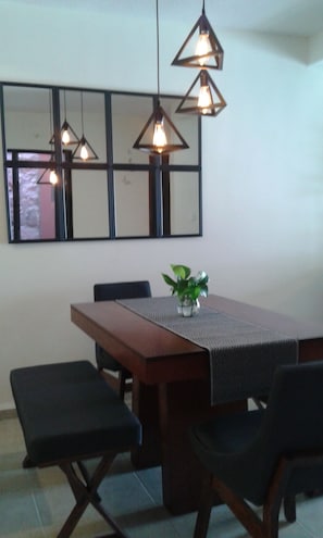 A dining area with a wooden table, four chairs, a vase with a plant, and three pendant lights.