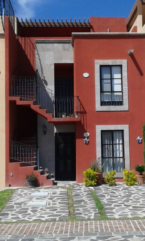 A two-story building with a red facade, a black door, and a small balcony with metal railings.