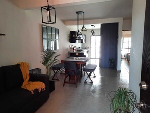 A modern living room with a black sofa, a dining table with chairs, and a kitchen area in the background.