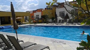 En swimmingpool med solstolar och parasoller, omgiven av byggnader med balkonger.