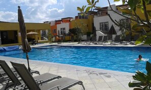 Une piscine entourée de bâtiments dotés de balcons, avec des chaises longues et des parasols à proximité.