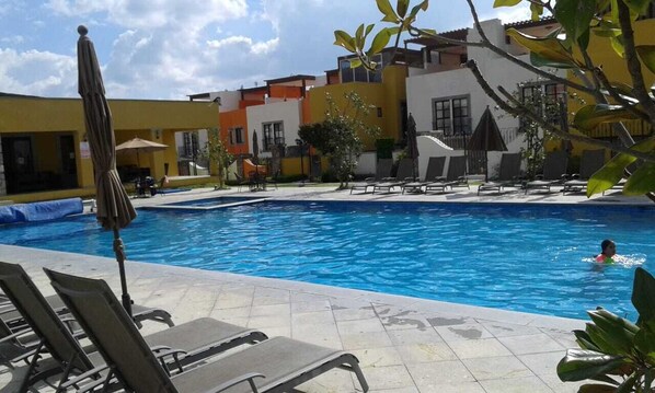A swimming pool with lounge chairs and umbrellas, surrounded by buildings with balconies.