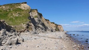 Ein felsiger Strand mit einer steilen Klippe und wolkenlosem, blauem Himmel.
