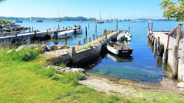 Ein Hafen mit Booten an Holzstegen, umgeben von Grünflächen und ruhigem Wasser.