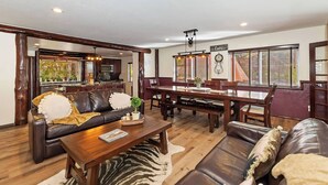 A spacious living room with a dark brown leather sofa, a wooden coffee table, and a dining area with a wooden table and chairs.