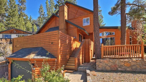 A log cabin with a stone foundation, wooden exterior, and a staircase leading to the entrance.