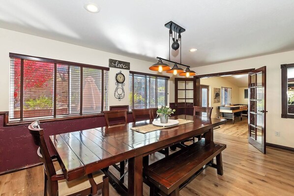 A spacious dining area with a long wooden table, multiple chairs, and a decorative clock on the wall.