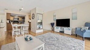Un salon moderne doté d’un téléviseur à écran plat, d’un canapé et d’un coin repas avec une table et des chaises blanches.
