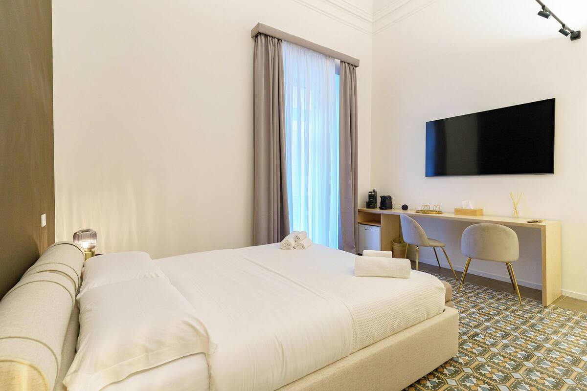 A hotel room with a bed, a desk, a chair, a TV, and a window with curtains.