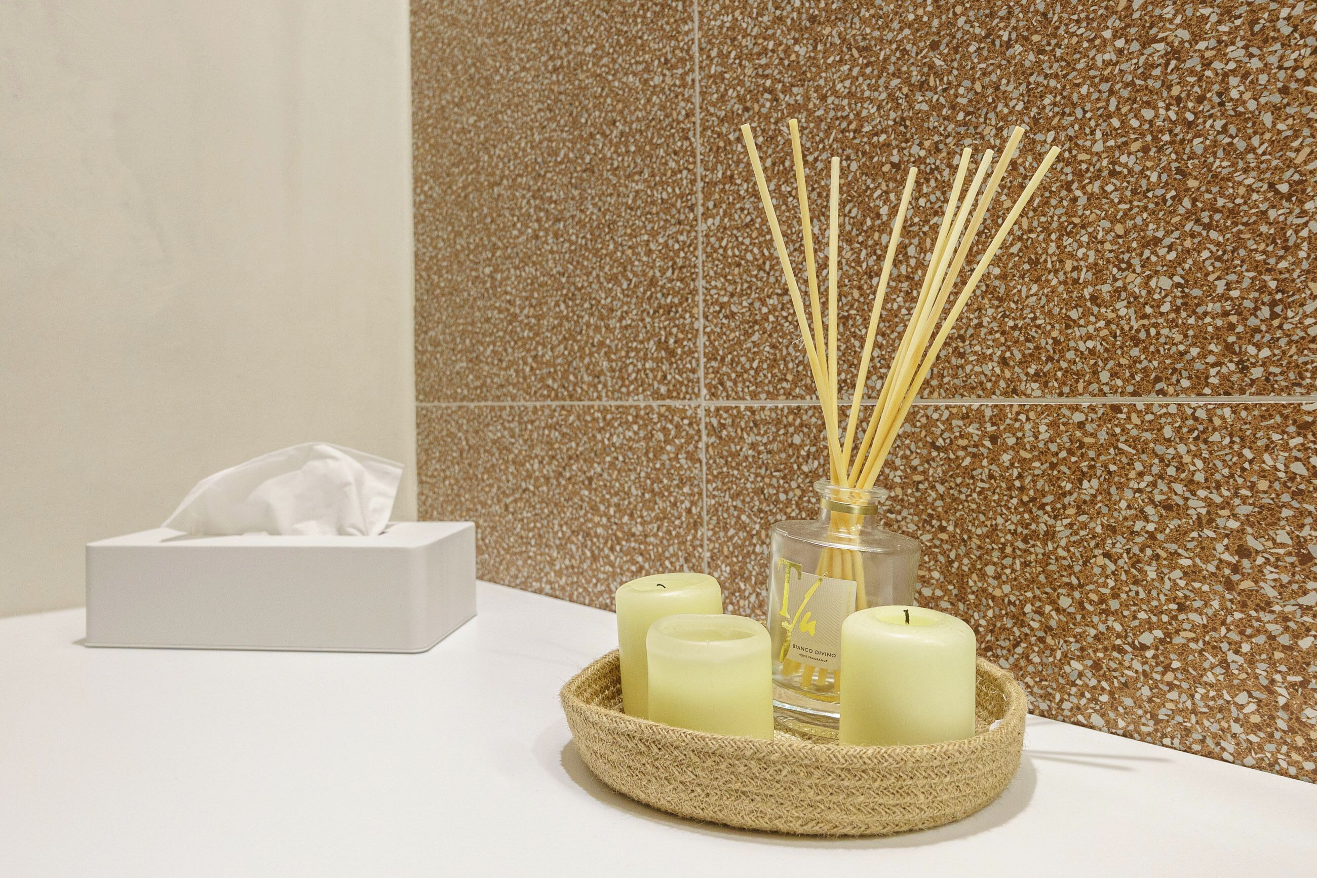 Une salle de bain avec un boîte de mouchoirs, des bougies et des diffuseurs à bâtonnets sur un comptoir blanc.
