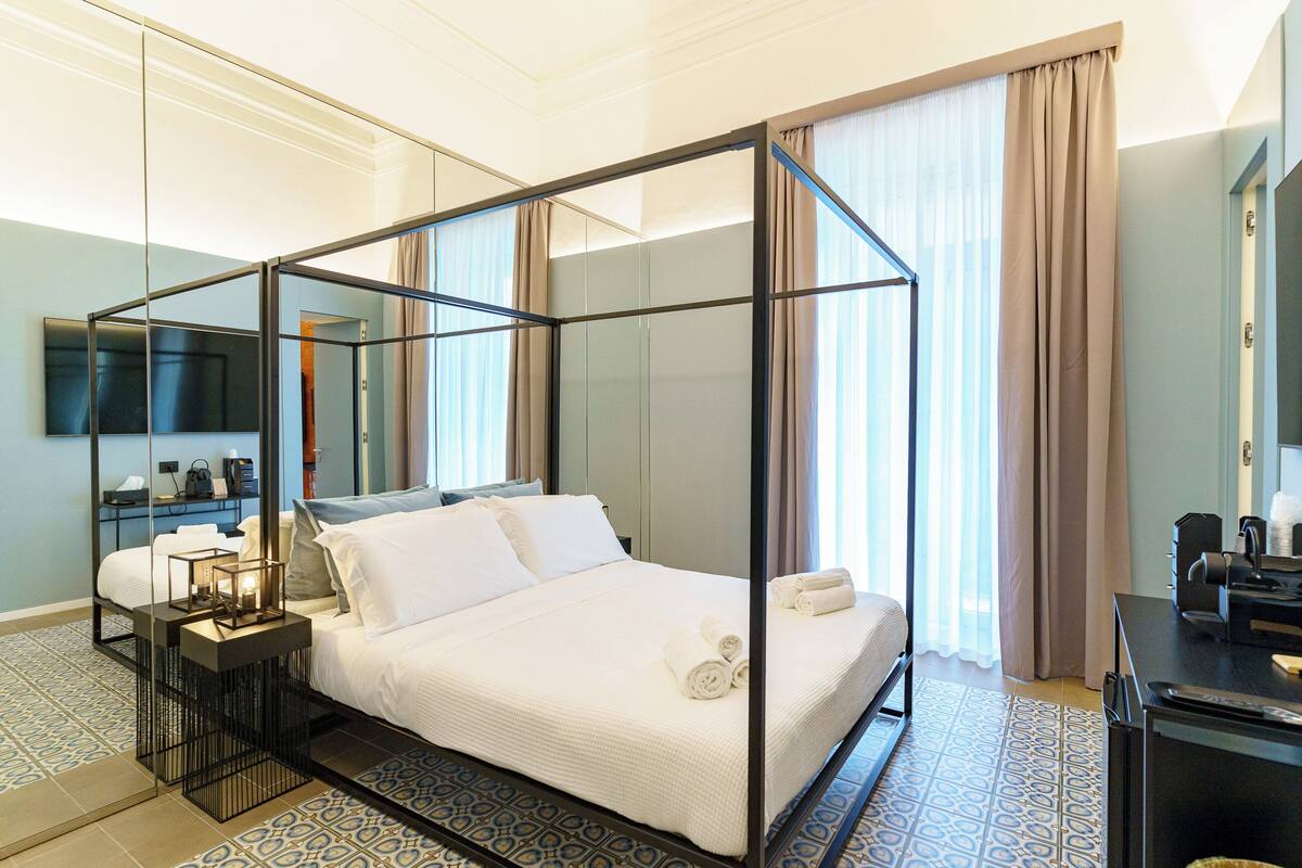 A four-poster bed with white linens, a bedside table with a lamp, and a desk with a chair.