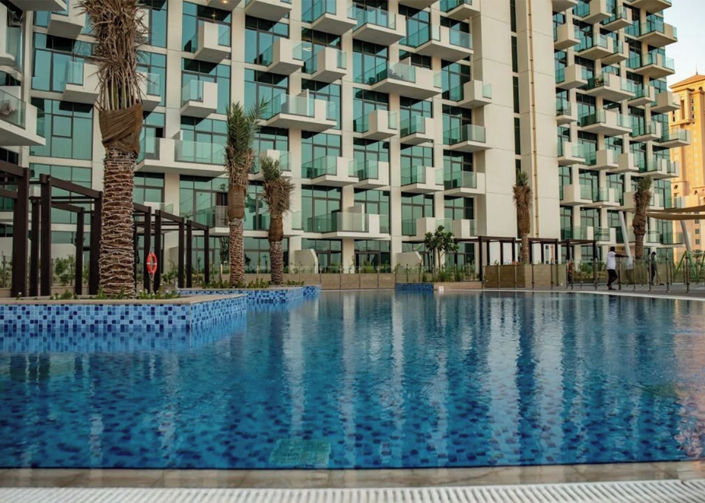 A modern hotel with a pool, multiple balconies, and palm trees.